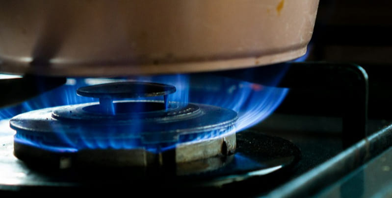 Working gas burner on stove. Blue flame with a saucepan sitting on top of it. 